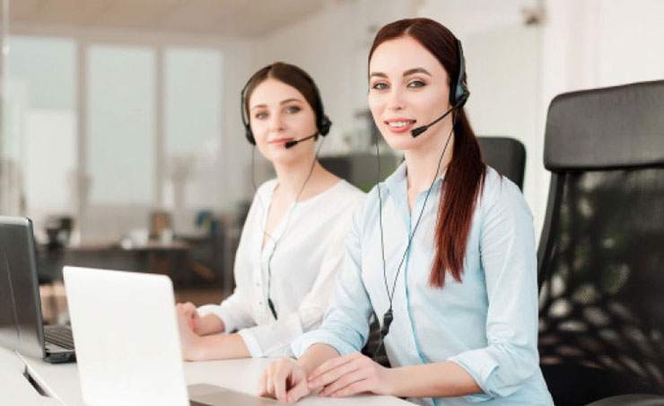 This image showcases two professional women in a modern office setting, wearing headsets and seated at desks with laptops.