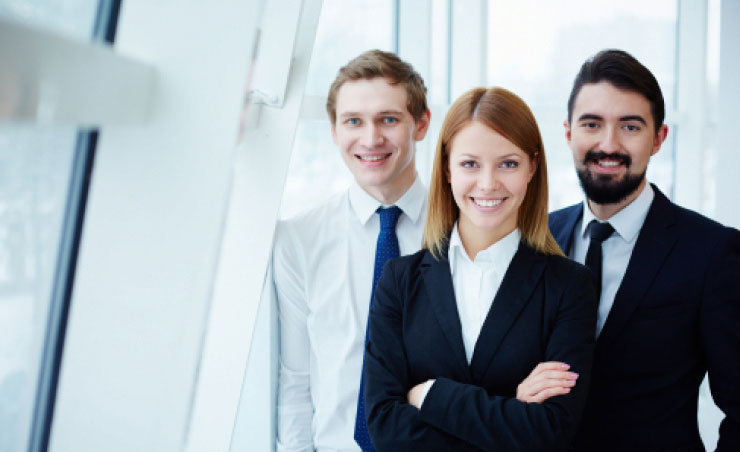 This image features a team of three professionals, dressed in business attire, standing together and smiling confidently.