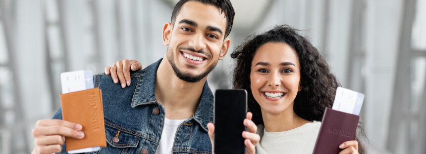 A smiling man and woman holding passports and boarding passes. They are excited and appear ready for travel.