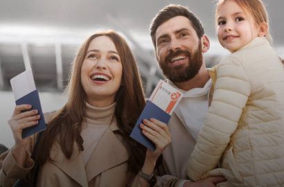 A happy family, consisting of a woman, a man, and a young girl, is at the airport. The parents are holding passports and boarding passes, ready for their trip.